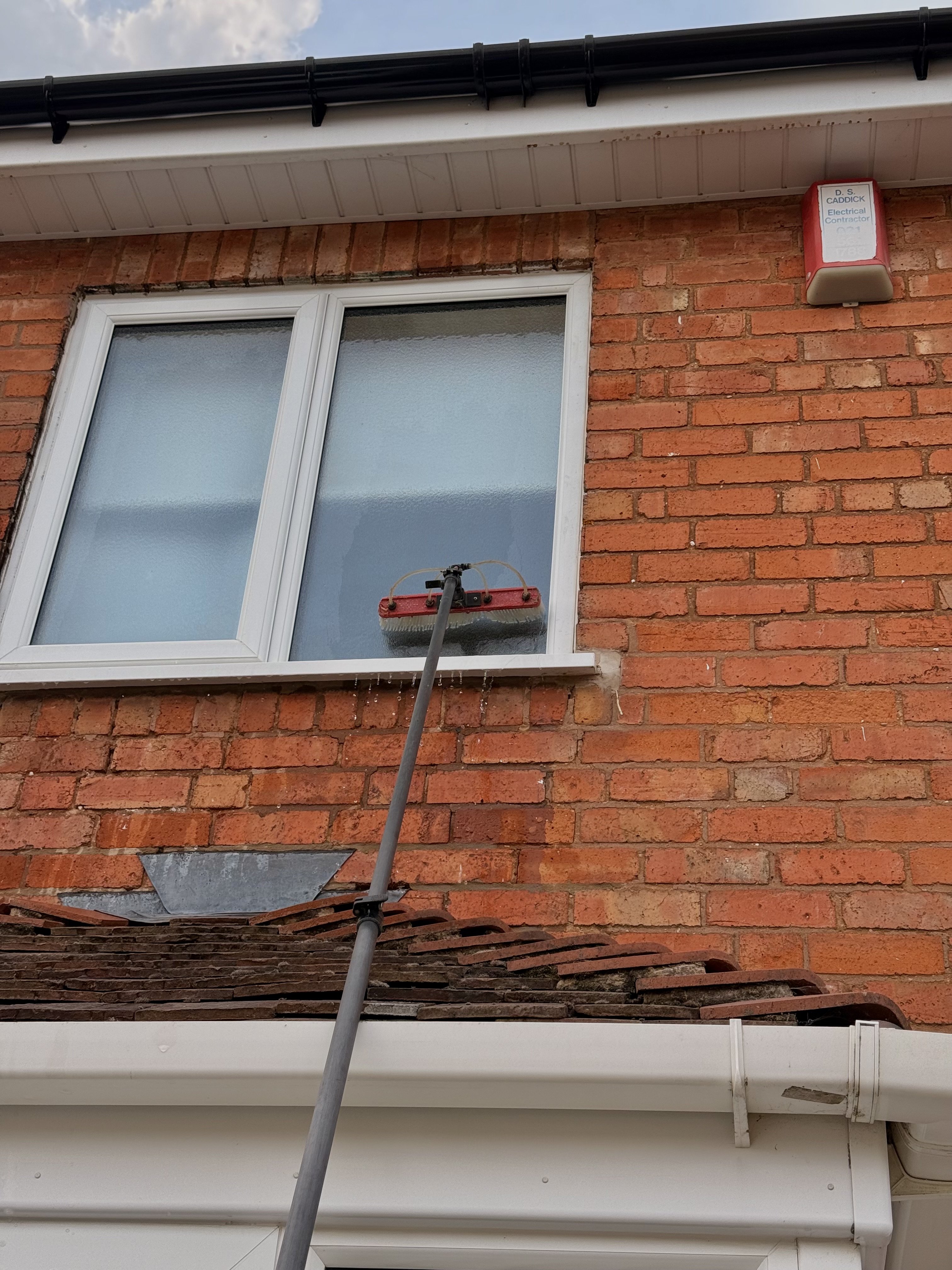 Water-fed brush cleaning an upper window from ground level